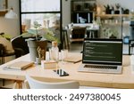 No people shot of modern laptop with code on screen, plants in pots, smartphone and glass bottle of water on desk in eco-friendly office