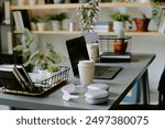 No people shot of part office interior with laptop, coffee cup, headphones and office supplies on desk, houseplants on shelves in background