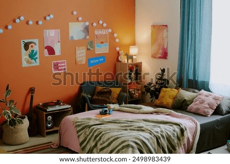 No people wide shot of modern teenagers bedroom interior with comfortable bed, posters and lights on orange wall, copy space