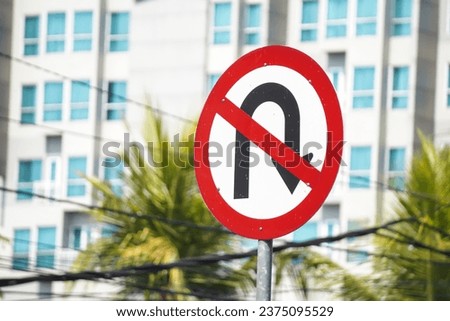 No right U turn sign on white colored board with cityscape backgrounds. Black arrow turn right allowed sign.