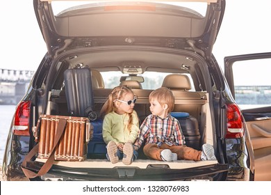 Keine Straße ist lang mit guter Gesellschaft. Kleine süße Kinder im Kofferraum eines Autos mit Koffern, die sich ansehen. Familienfahrt