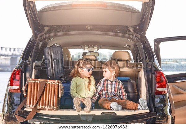No road is long with good company. Little cute kids\
in the trunk of a car with suitcases looking at each other. Family\
road trip