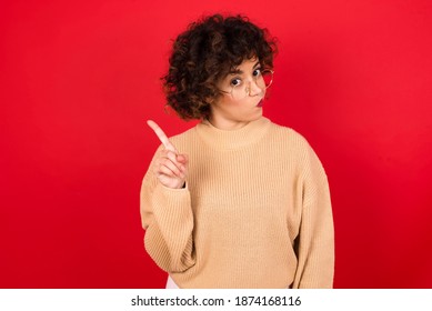 No sign gesture. Closeup portrait unhappy Young beautiful Arab woman wearing knitted sweater standing against red background raising fore finger up saying no. Negative emotions facial expressions.