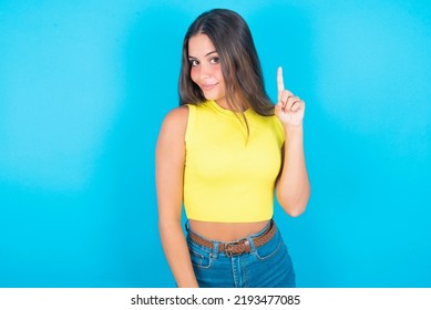 No Sign Gesture. Closeup Portrait Unhappy Beautiful Brunette Woman Wearing Yellow Tank Top Over Blue Background Raising Fore Finger Up Saying No. Negative Emotions Facial Expressions, Feelings.