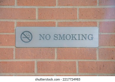 No Smoking Sign Debossed On A Metal Plate Against Brick Wall Of A Building. Outdoor Views In Austin Texas With Close Up Of A Signage Prohibiting Use Of Cigarette In The Area.