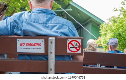 A NO SMOKING Sign On The Back Of A Wooden Bench At An Outdoor Concert Venue.