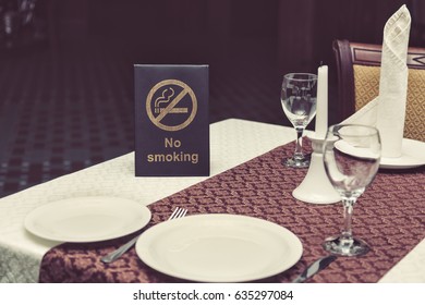 No Smoking Sign On Table With Glasses, Napkin And Plates In Restaurant.