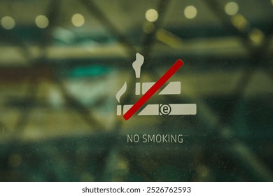 a No Smoking sign and sticker on the window with a blurred background of a park. Some copy space.