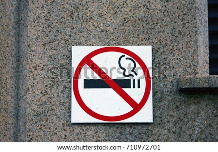 no smoling sign with strikeout black cigarette in red circle on white background on granite wall of building