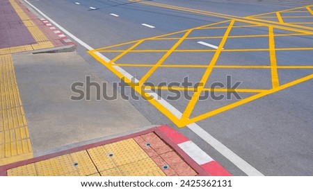 No stopping yellow crisscross zone traffic sign on asphalt road surface at the entrance or exit way of hospital with yellow tactile paving line for the blind and visually impaired on sidewalk