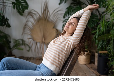 No stress. Serene young Polish girl resting in tropical indoor garden, peaceful Italian female relaxing with closed eyes, stretching arms, enjoying peace in tropical oasis of urban jungle interior
