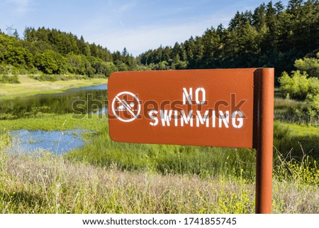 No swimming sign posted on the shoreline of a mountain lake covered in aquatic vegetation, California
