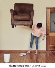 No Task Is Too Difficult For Her. Shot Of A Woman Lifting A Couch To Mop Underneath It.