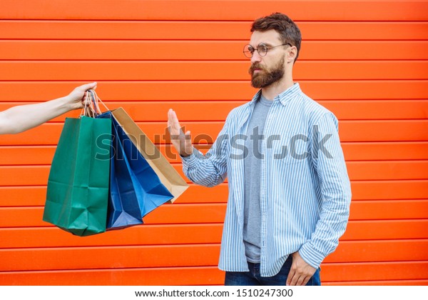 No thanks. rejection refusal and denial. Man\
putting hands forward pushing stretching hand with paper bags\
Portrait of a bearded guy on red background.Negation,negative,stop\
shopping, no sale concep