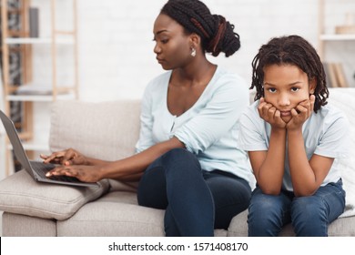 No Time For Child. African Mom Is Busy Working At Home On Laptop, Sad Bored Daughter Nearby. Free Space