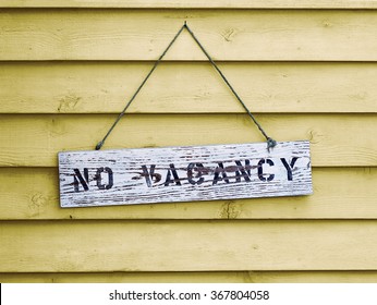No Vacancy sign hanging on yellow painted cedar siding.
