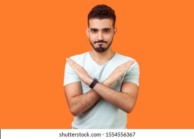 No way, absolutely not. Portrait of determined brunette man with beard in white t-shirt showing x sign with crossed hands, meaning stop, this is the end. studio shot isolated on orange background