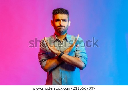 No way, absolutely not. Portrait of man in shirt showing x sign with crossed hands, meaning stop, this is the end. Indoor studio shot isolated on colorful neon light background.