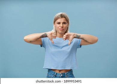 No Way Mate Dislike. Portrait Of Dissatisfied Bossy Female Tattoo Artist With Tattoos On Arms Frowning From Displeasure Showing Thumbs Down In Disapproval Standing Over Blue Background
