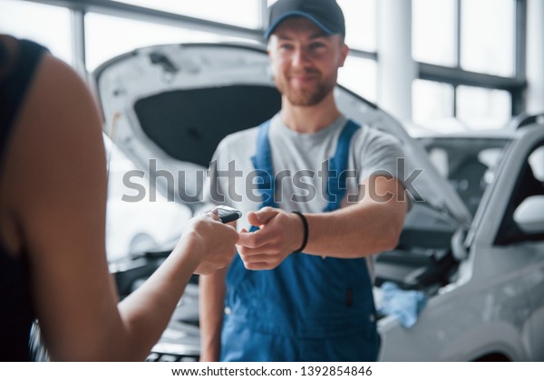 No\
worries, everything will be okay. Woman in the auto salon with\
employee in blue uniform taking her repaired car\
back.