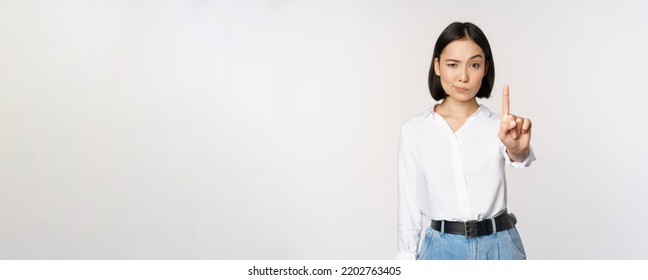 No. Young Serious And Confident Asian Woman Showing Stop, One Finger Gesture, Taboo Sign, Standing Over White Background