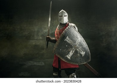 Noble warrior. Portrait of one medeival warrior or knight in armor and helmet with shield and sword posing isolated over dark background.