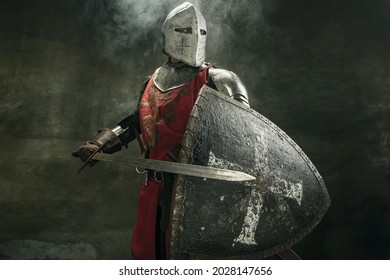 Noble warrior. Portrait of one medeival warrior or knight in armor and helmet with shield and sword posing isolated over dark background. - Shutterstock ID 2028147656