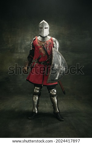 Noble warrior. Portrait of one medeival warrior or knight in armor and helmet with shield and sword posing isolated over dark background.