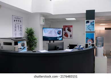 Nobody In Hospital Waiting Room Front Desk With Office Supplies And Promotional Flyers In Healthcare Facility. Empty Reception Counter With No People At Private Practice Clinic.