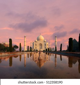 Nobody present as Taj Mahal glows beautifully at sunset reflected in front garden water fountain pool of water under a dramatic pink sky in Agra, Uttar Pradesh, India. Plenty of copy space