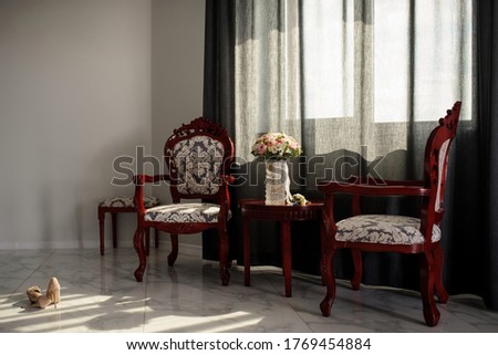 Nobody in the room with old vintage wood chairs and table. On the table a flowers bouquet and hear a pair of women shoes