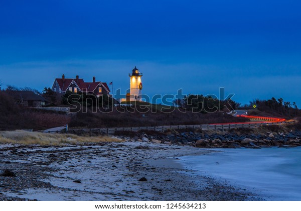 Nobska light house in Woods Hole Mass lit up\
with christmas wreath as a car\
passes