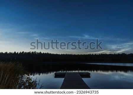 Noctilucent clouds over the forest lake in Latvia at July night. Wooden pier on foreground.