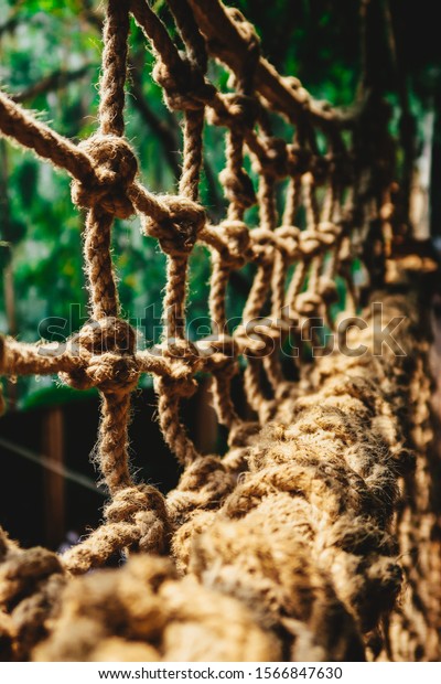 Nodal bridge of braided ropes from a\
close distance part of the edging of the handrail of the bridge\
with a gradual blur of focus. Part of a braided rope\
bridge