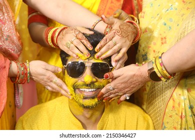 Noida, India 2022: Ladies applying turmeric paste during haldi ceremony to groom. He is wearing sub glasses and smiling 