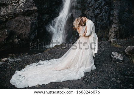 noise effect, selective focus: Wedding. The guy and the girl in a dress standing against a background of high mountains and holding hands, she is holding a bouquet