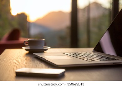 Nomad work Concept Image Computer Coffee Mug and Telephone large windows and sun rising, focus on laptop touch pad 