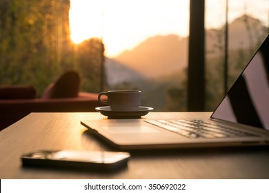 Nomad Arbeit Concept Image Computer Kaffee Umarmung und Telefon große Fenster und Sonne aufgeht, Fokus auf Kaffeekrug