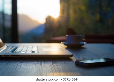 Nomad Work Concept Image Computer Coffee Mug And Telephone On Black Wood Table And Evening Sunlight Shining Throw Large Windows Focus On Edge Of Laptop