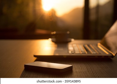 Nomad Work Concept Image Computer Coffee Mug And Telephone On Black Wood Table And Evening Sunlight Shining Throw Large Windows Focus On Phone