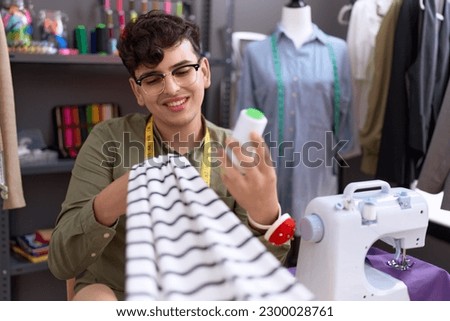 Non binary man tailor smiling confident holding cloth and thread at atelier
