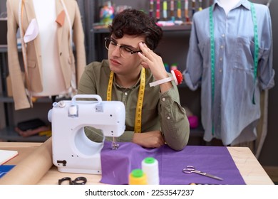 Non binary man tailor stressed using sewing machine suffering for headache at atelier