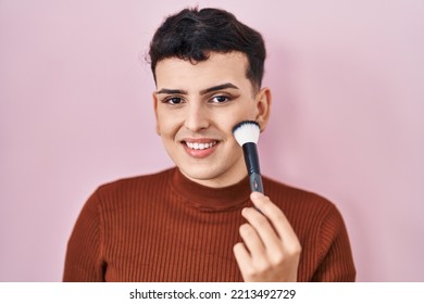 Non binary person applying make up looking positive and happy standing and smiling with a confident smile showing teeth 