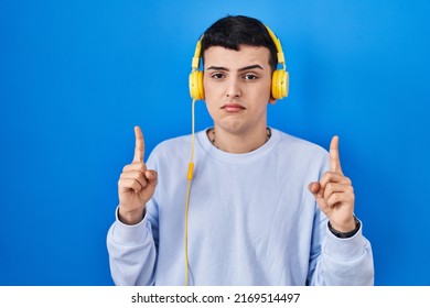 Non Binary Person Listening To Music Using Headphones Pointing Up Looking Sad And Upset, Indicating Direction With Fingers, Unhappy And Depressed. 