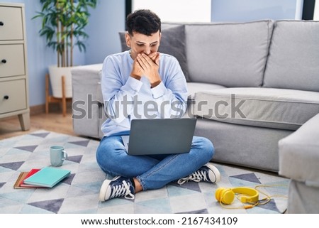 Non binary person studying using computer laptop sitting on the floor shocked covering mouth with hands for mistake. secret concept. 