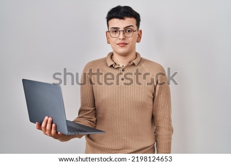 Non binary person using computer laptop relaxed with serious expression on face. simple and natural looking at the camera. 