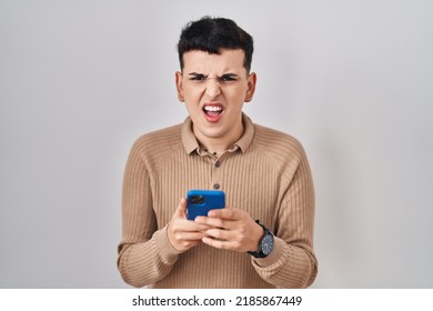 Non Binary Person Using Smartphone Typing Message Angry And Mad Screaming Frustrated And Furious, Shouting With Anger. Rage And Aggressive Concept. 