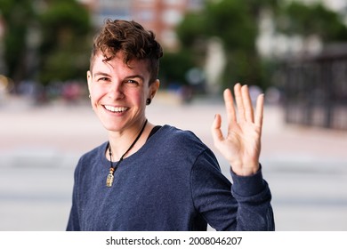Non binary transgender Tomboy looking at camera, greeting and waving hand smiling during internet online communication.