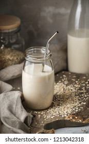 Non Dairy Oat Milk In Glass Jar With Metal Reusable Drinking Straw On Rustic Background. Oat Flakes Scattered On The Table.