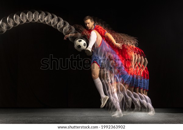 Non stop moving. Young caucasian football soccer\
player playing with ball in motion in mixed light on dark\
background. Concept of healthy lifestyle, professional sport,\
action, motion, hobby,\
team.
